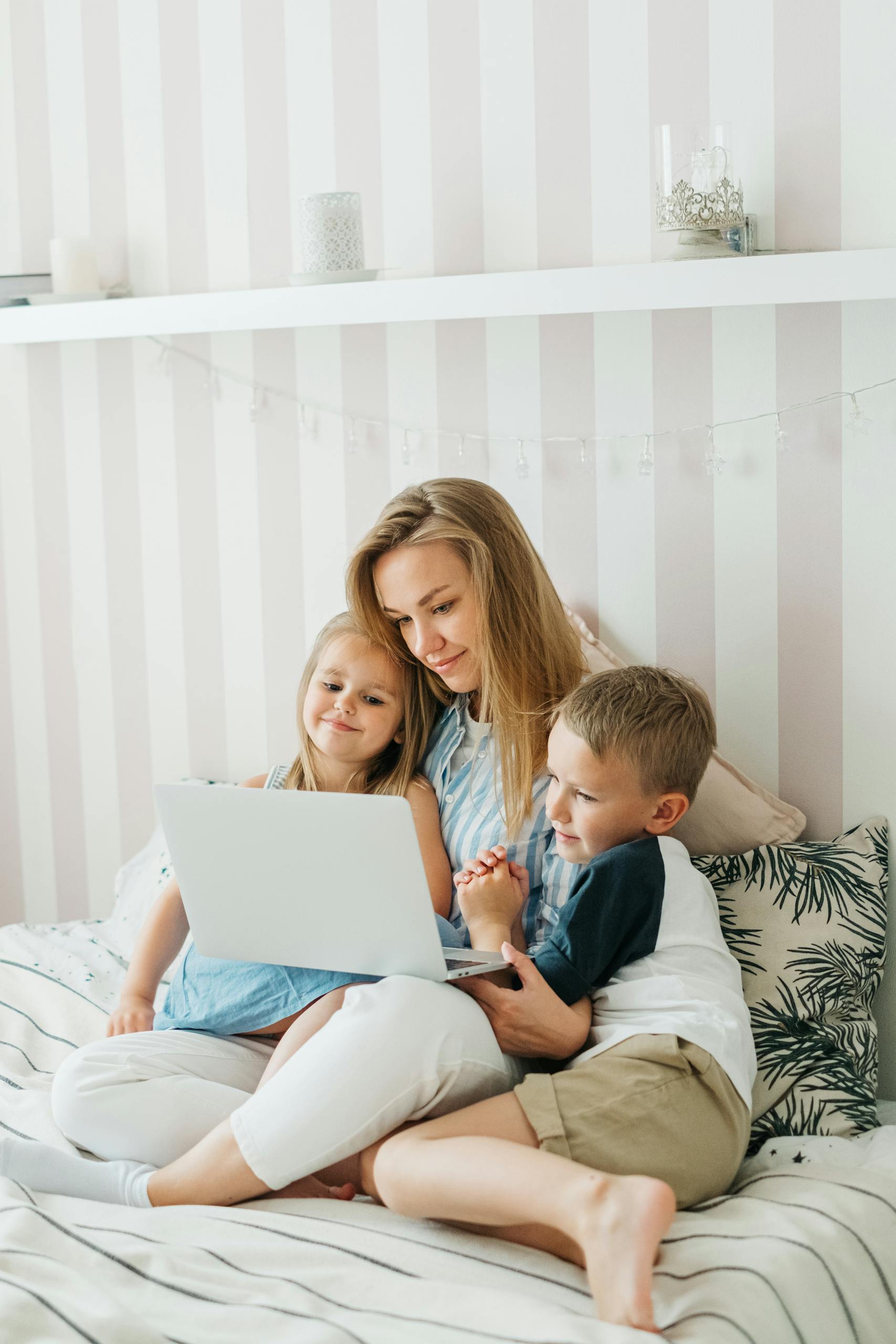 Links 11 A mother sits on a bed with her children, sharing a joyful moment using a laptop.