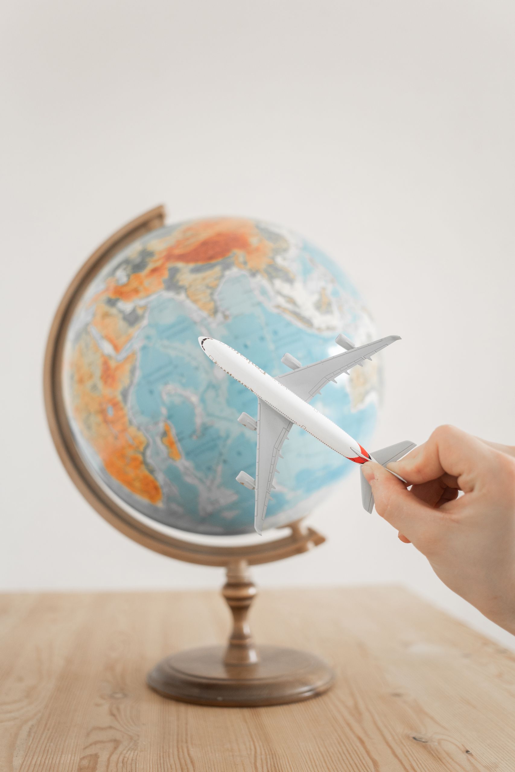PGD and IVF 8 Close-up of a hand with a toy airplane in front of a globe, symbolizing travel and exploration.