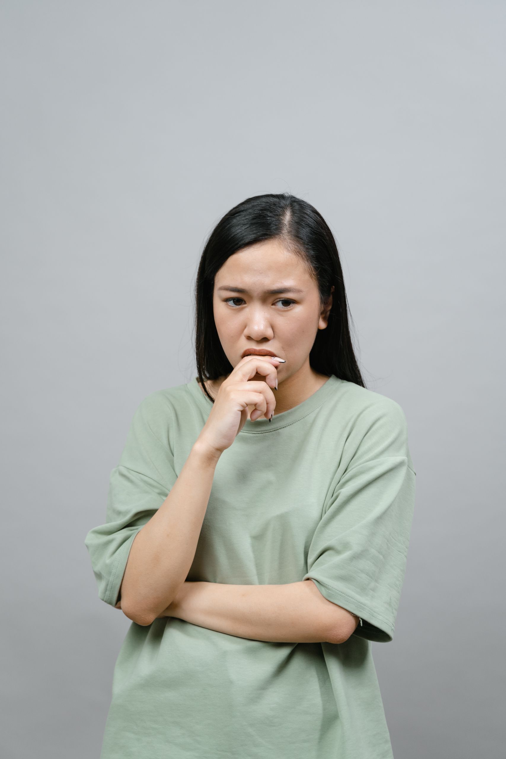 PGD and IVF 9 Portrait of an Asian woman in a green shirt looking thoughtful against a gray backdrop.